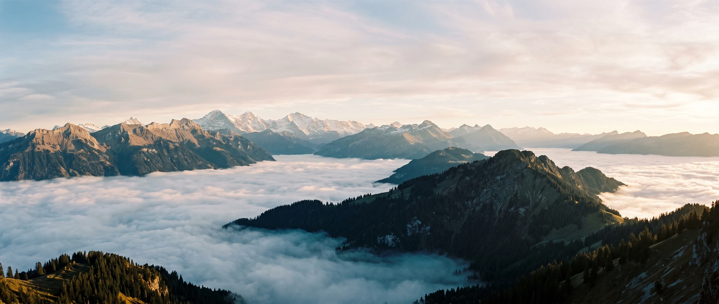 Blick über ein Nebelmeer auf eine Kette verschneiter Gipfel im Morgenlicht