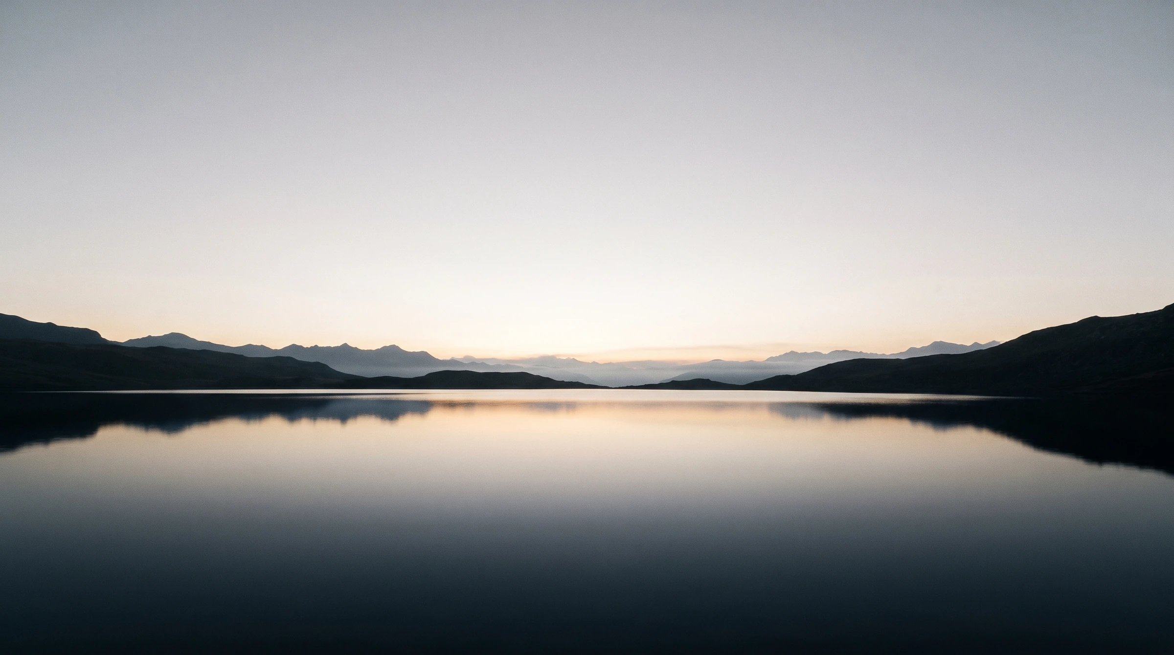 Alpensee im Morgenlicht, gestaffelte Bergrücken, Dunst über dem Wasser