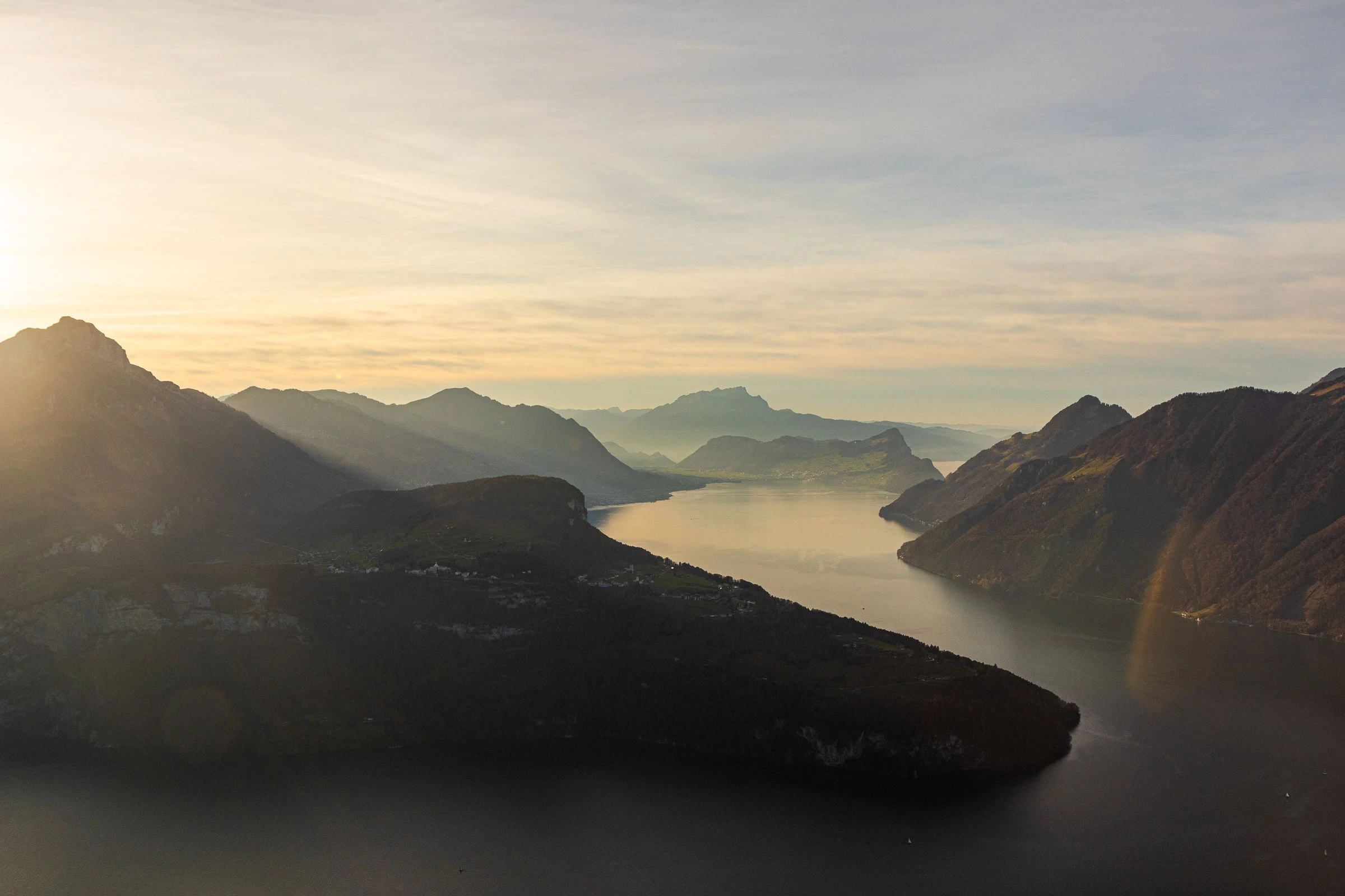 Alpensee im Morgenlicht, gestaffelte Bergrücken, Dunst über dem Wasser